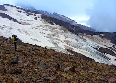 A man hikes along a rocky ridge next to a glacier.
