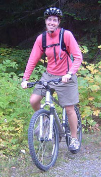 A bicyclist, wearing a helmet and backpack, sits on her bicycle on Westside Road.