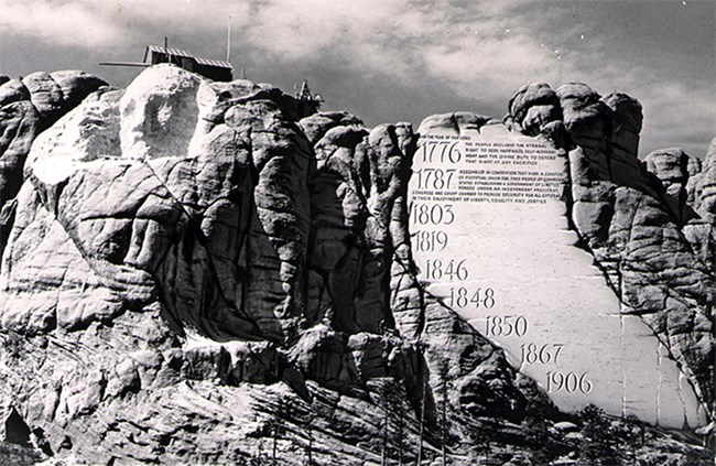 Image of Mount Rushmore as carving began with only George Washington's face started towards the left.  The Entablature is seen on the right as a conceptual drawing added to the photo.