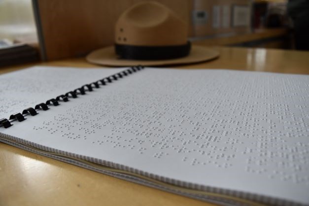 Mount Rushmore braille brochure on desk with brown park ranger flat hat in background