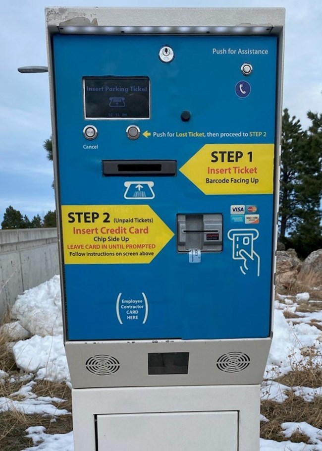 Closeup view of a parking facility exit station.  The station has a blue panel with step-by-step instructions for using a ticket to exit and paying for parking.