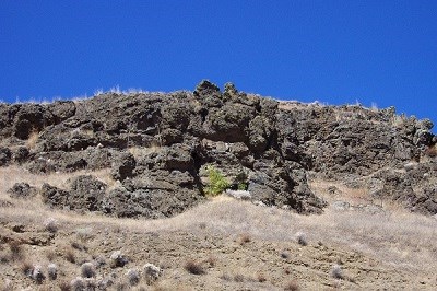 A basaltic rock outcropping on a hillside on a sunny day.