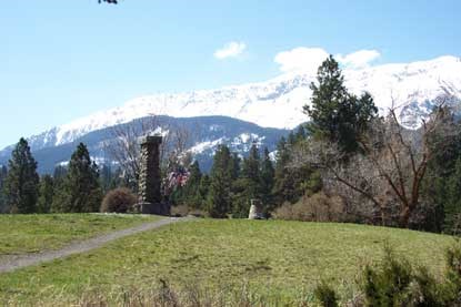 A grave and monument on top of a hill with the mountains in the background.