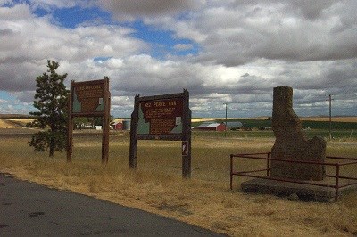 A highway pullout with two interpretive signs and a monument in the shape of Idaho on a cloudy day.