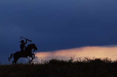 A metal silhouette of a Nez Perce warrior on horseback with the sunset in the background.