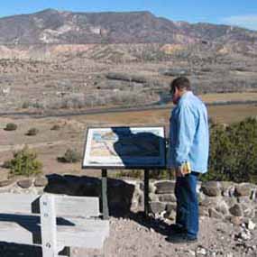 A visitor stands before an outdoor wayside exhibit with an open view of New Mexico landscape.