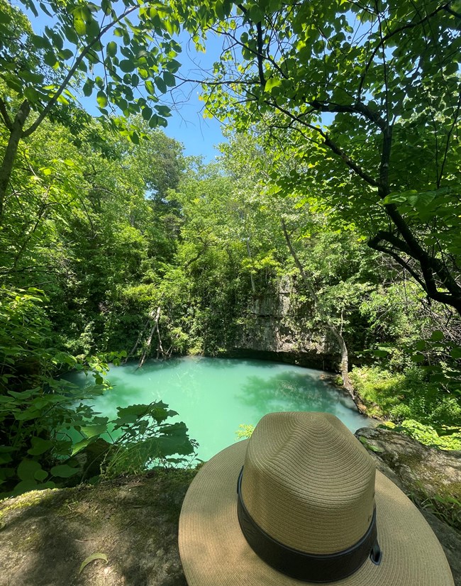 A straw ranger hat sits on a rock above a large, round spring.