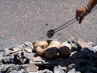 several pots are manipulated by tongs in a firepit