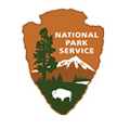 The National Park Service logo is an arrowhead with a brown background, featuring snow capped mountains and a buffalo.