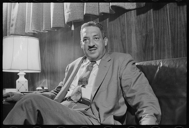 An historic photo of an older African American man in a suit, sitting on a couch.