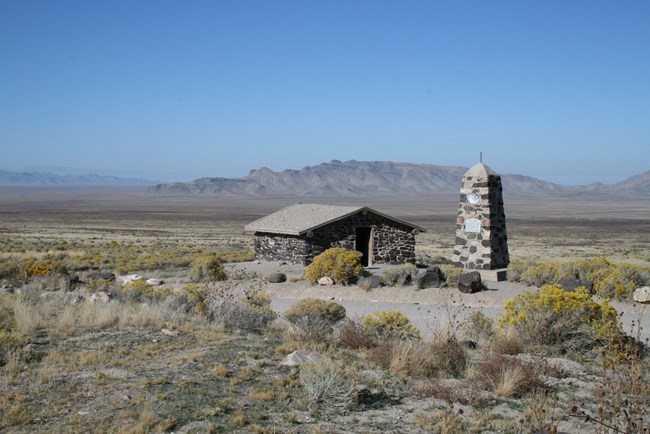 A stone cabin sits in a wide open, high desert plain.