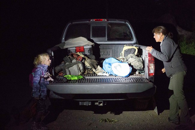 A little girl and a scientist talk to each other across the back of a pickup truck.