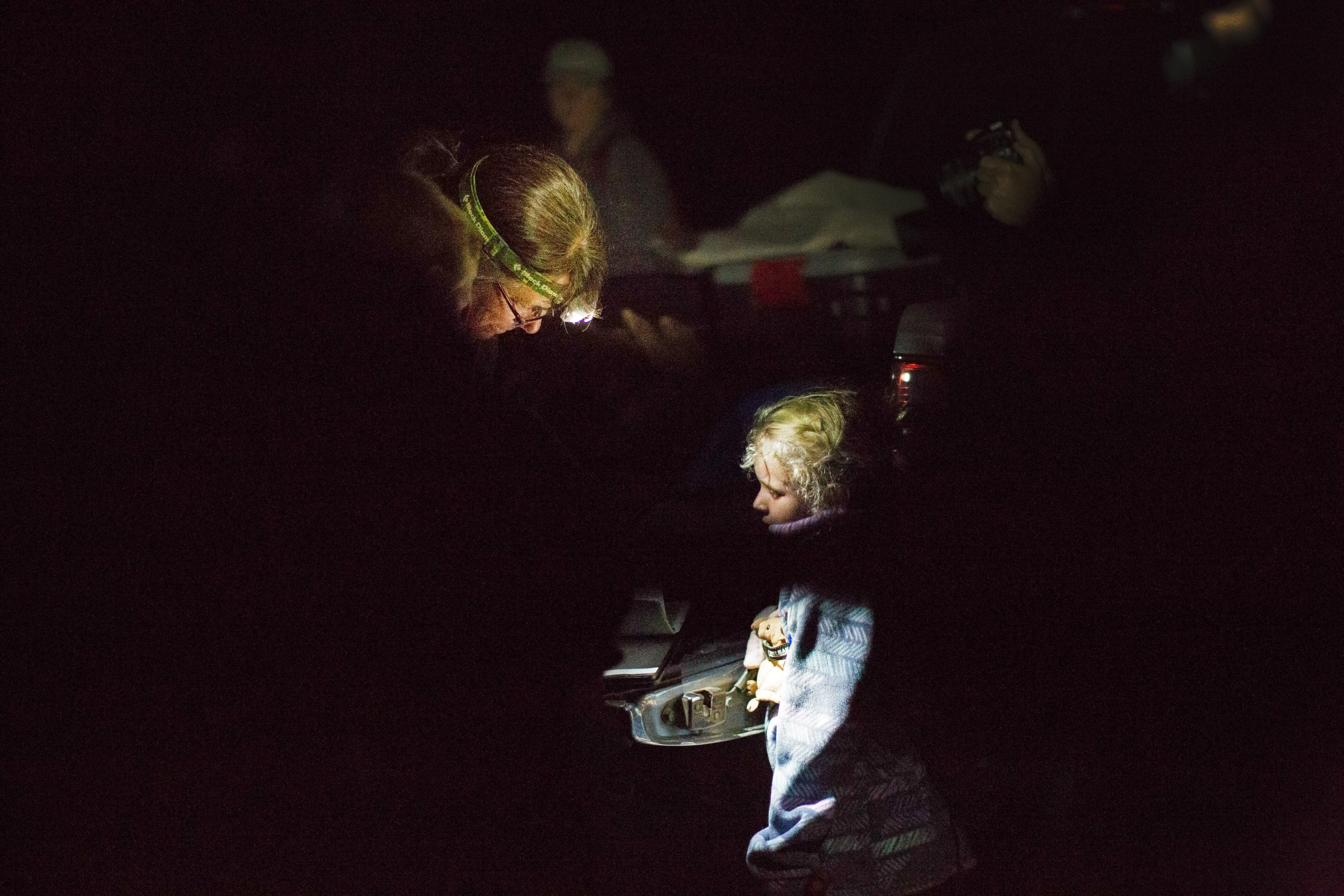 Illuminated by headlamp, a woman scientist shows the little girl a bat.