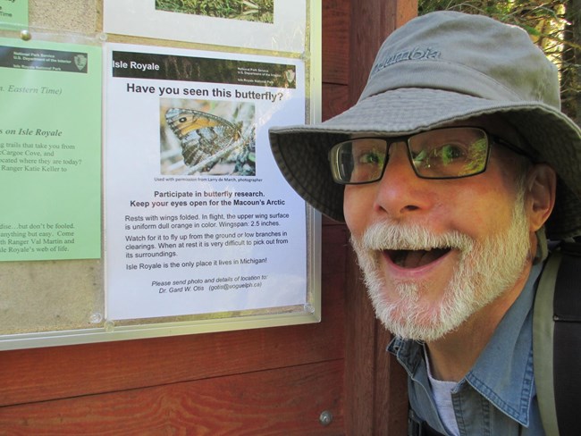 A man standing next to a poster about he Macoun's Arctic butterfly smiles at the camera.