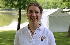 A woman in a National Park Service polo shirt smiles. She is wearing a bat necklace and earrings.