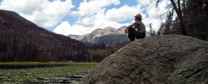 A ranger sits next to a mountain lake