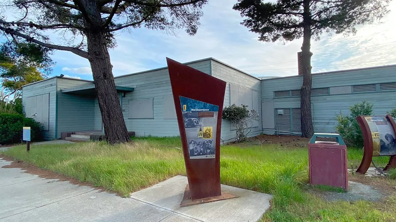 A one-story building with wear and tear. A metal interpretive sign in front.