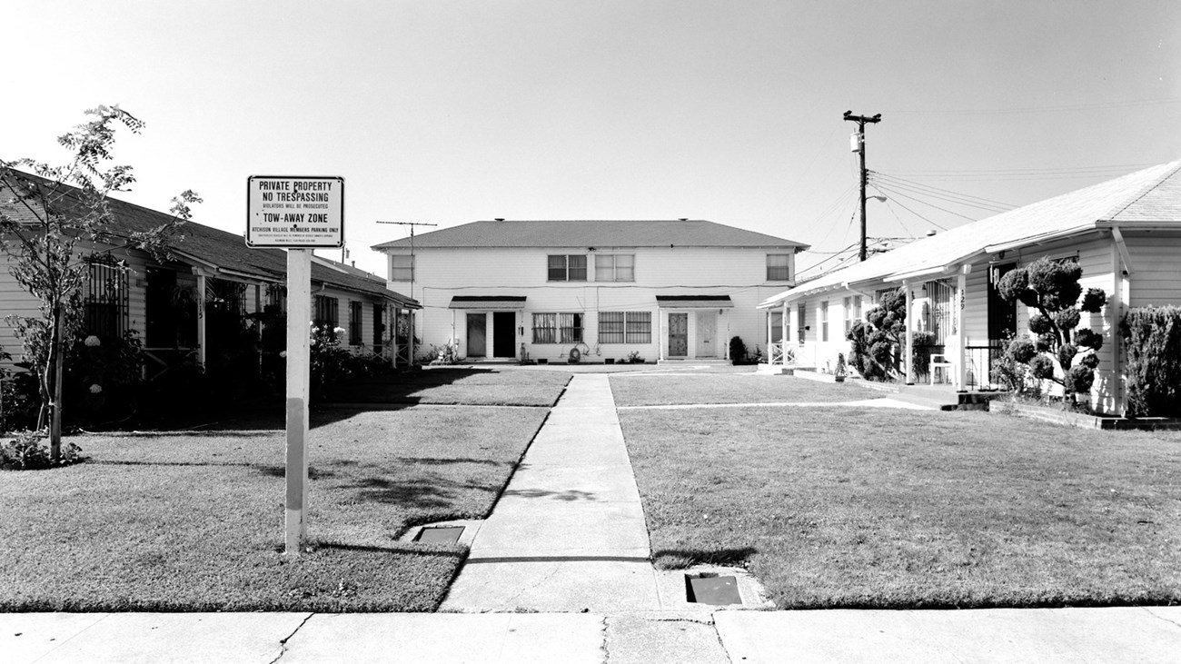 Historic photos of multiple two-story housing buildings. Sidewalk leads to building.