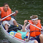 Close up of two boyscouts wearing orange lifejackets canoeing on the river.