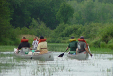 Three aluminum canoes travel down river with young men in lifejackets paddling