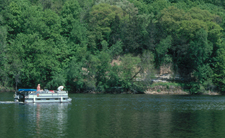 High sandstone banks with trees frame a pontoon boat on the river