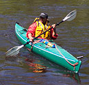 A turquoise kayak, orange jacket and yellow lifevest makes for a colorful picture of a woman paddling a kayak.