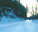 A snowy foreground with ski tracks and a skier in the distance on the ice by a rock cliff.