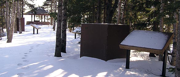 Footsteps travel in the snow near waysides and statues covered for winter.
