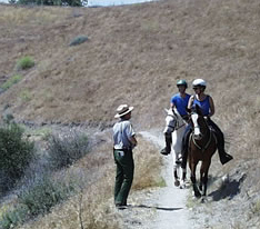 Ranger stands next to trail and talks to two equestrians.