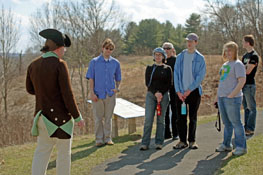 A Battlefield Guide in Revolutionary War American uniform speaks with a group of visitors.