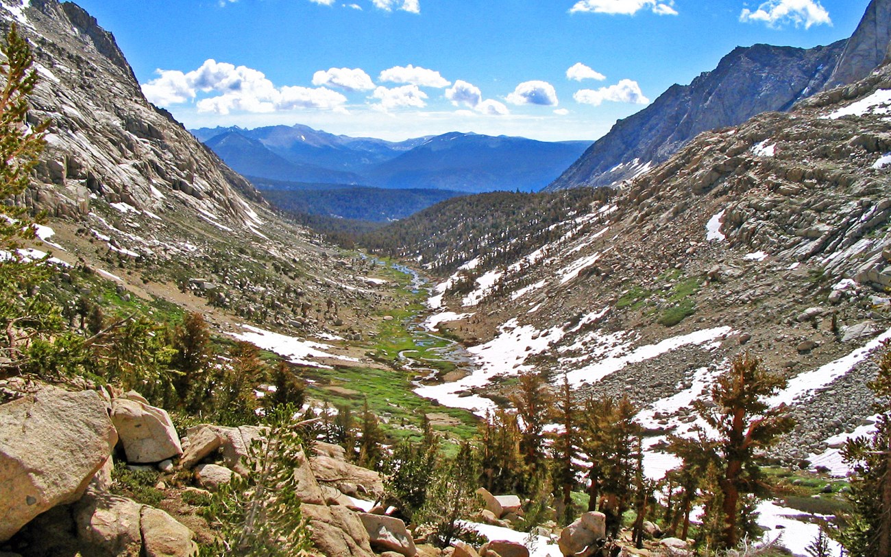 a mountainous u-shaped valley with scattered snow and trees