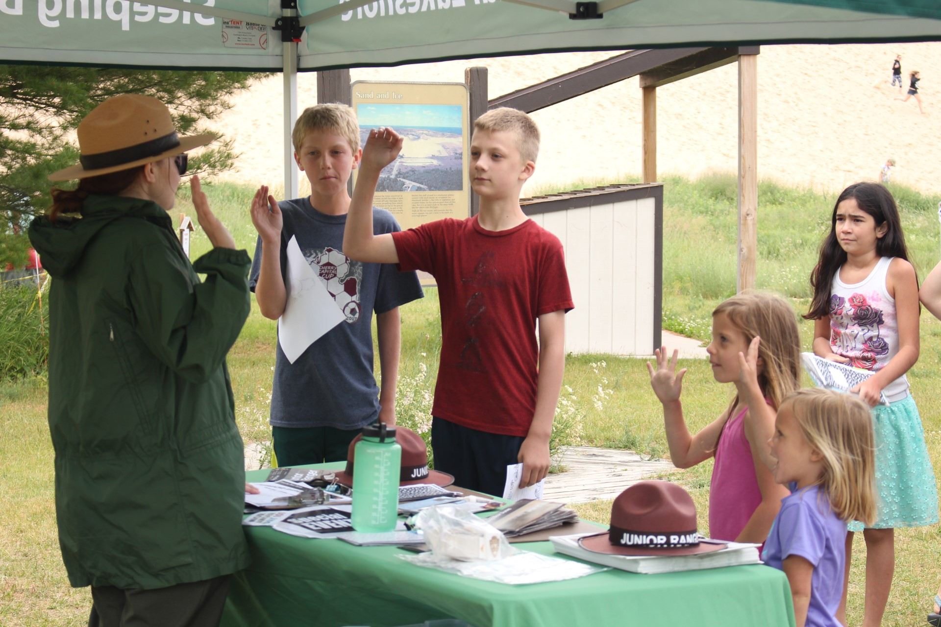 A park ranger swears in four Junior Rangers at the Dune Climb while a girl watches in the background.