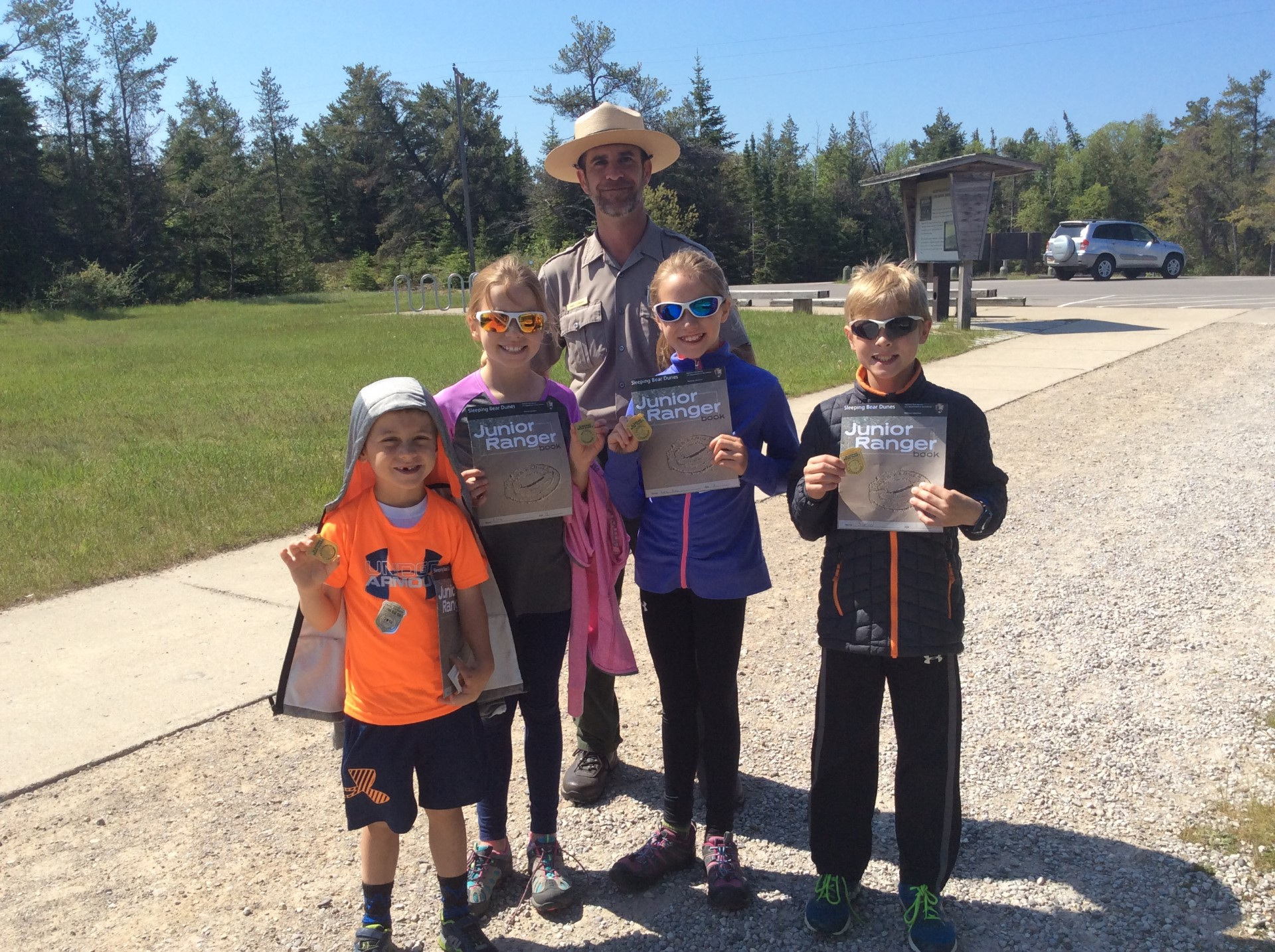 Four Junior Rangers smile and hold their badges and completed books up in front of a smiling park ranger.