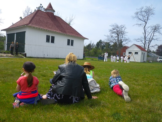 A family sits on the grass and watched kids and rangers reenact a shipwreck rescue