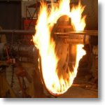 flames envelope a spoked locomotive wheel as a tire is heated, expanded, and placed on the wheel.