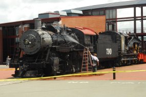 A contractor pressure washes a black locomotive on display near the Steamtown NHS Visitor Center.