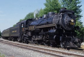 A steam locomotive pulls dark green passenger cars through the Northeast Pennsylvania forest.