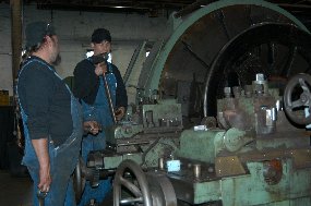 Two of Steamtown's mechanics trim railroad wheels on a large lathe.