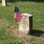 American flag in front of a national cemetery headstone.