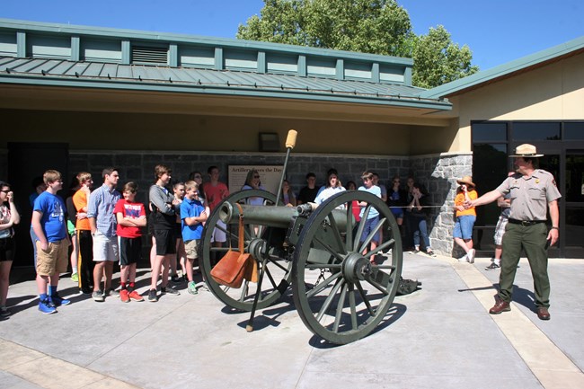 A park ranger holds a lanyard connected to a cannon in front of a group of students.