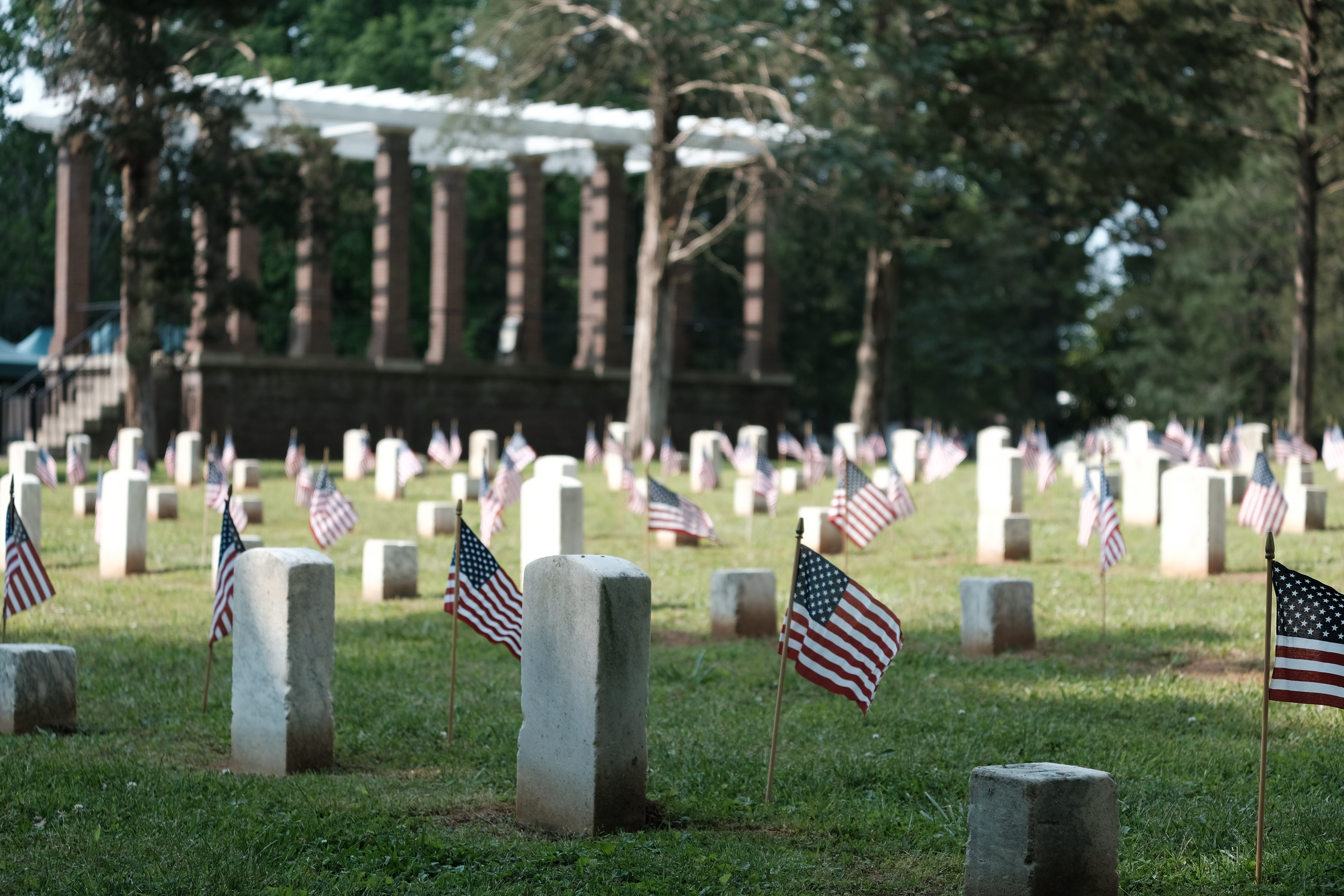 American flags stand in front of headtsones arrayed in rows.