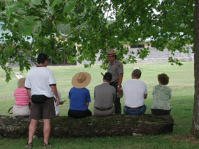A park ranger talks to visitors sitting on a log.