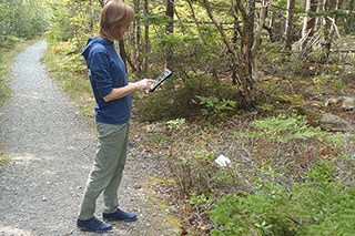 A woman holds an iPad looking at vegetation