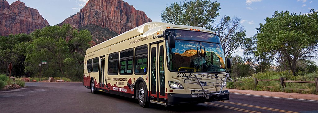 A large, new bus in the foreground with sandstone peaks in the background