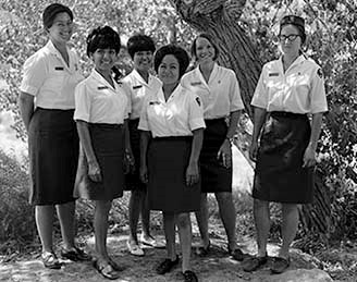 Six Women guides and rangers in white shirts and dark skirts standing under a tree.