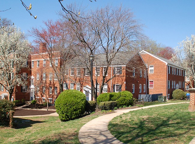 Red brick buildings with white-framed windows, surrounded by spring foliage and a curving walkway.