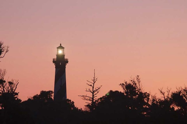 lighthouse at sunset with trees in the foreground