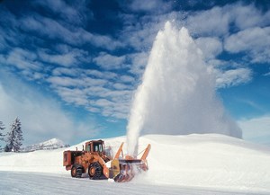 A snowplow blows snow off of a road.