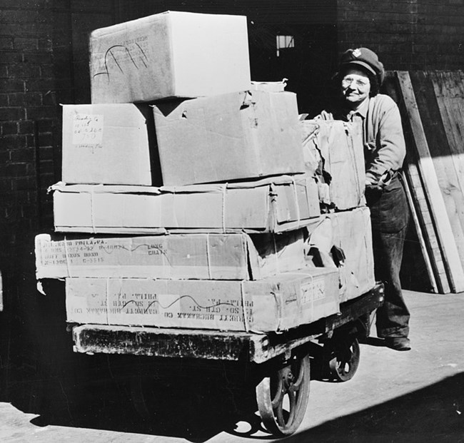Woman pushing a cart of boxes and trunks.