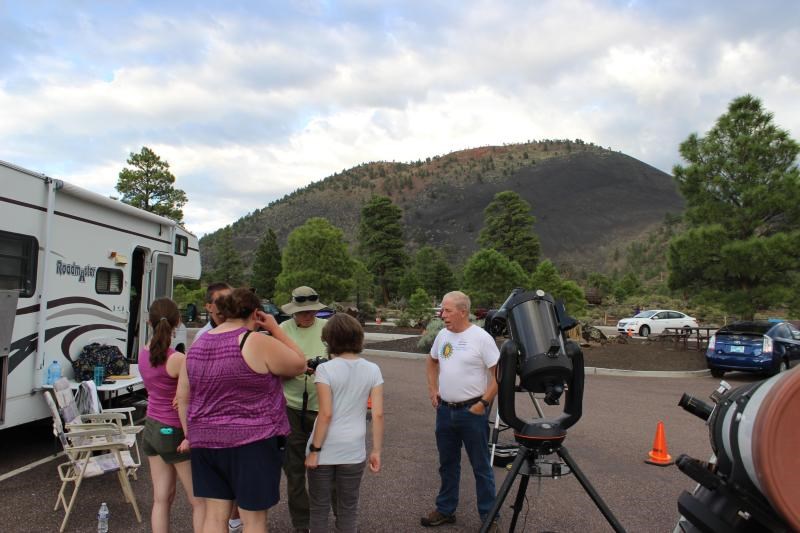 Volunteer astronomers speaking with visitors near telescopes, with Sunset Crater Volcano in the background.